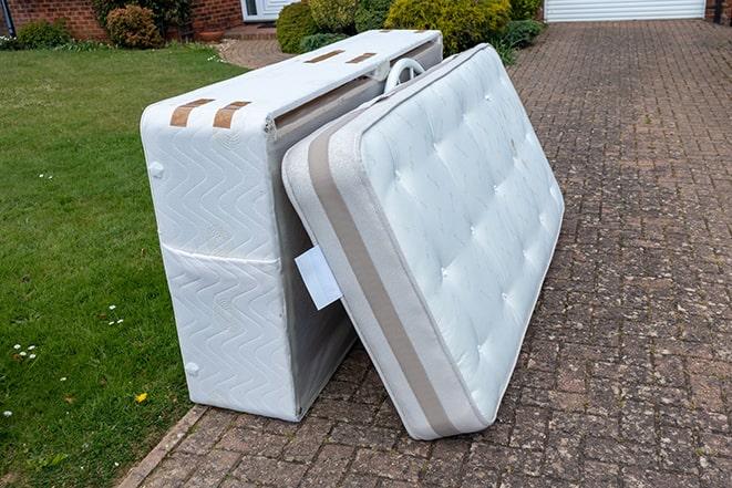 man carrying a rolled-up mattress out of a house